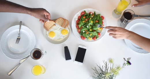 People eat a healthy meal, in the middle of the table there is a telephone and the device